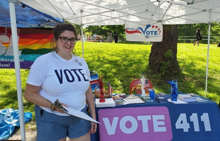 A woman standing in front of a tent with a sign that says Vote 411.